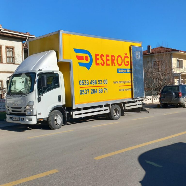 Sokakta park halinde duran sarı renkli Eseroğlu Nakliyat & Depolama logolu taşımacılık kamyonu
